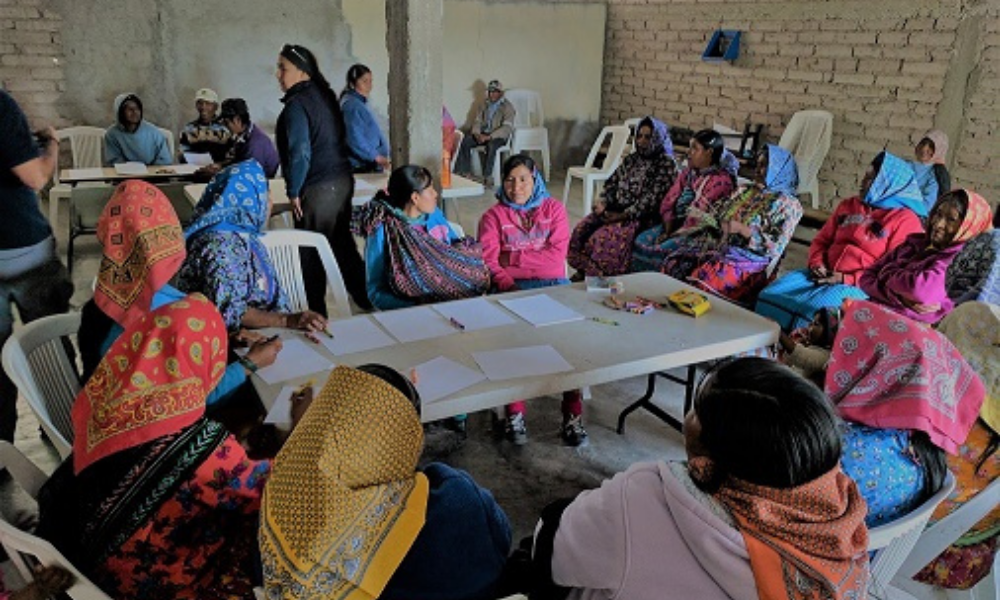 A group of women wearing traditional clothing, sitting around a table, discussing tourism initiatives. 