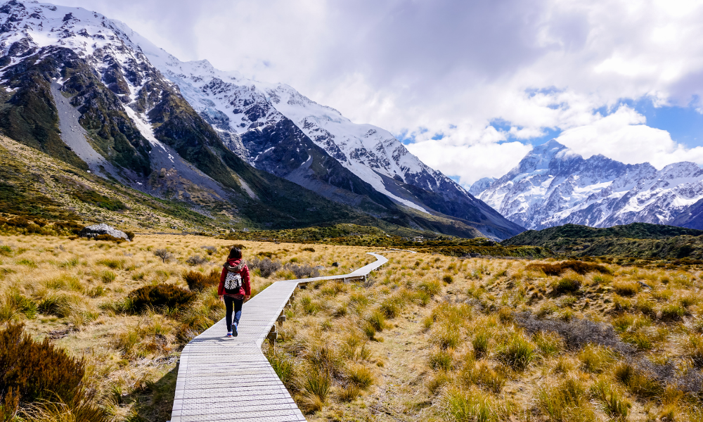 A hiker on a trail surrounded by snow-capped mountains.