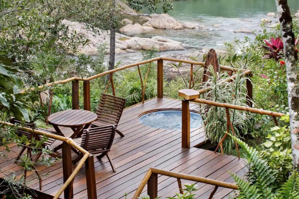 wooden deck with wooden patio chairs and table, a sunken round pool in patio deck, all overlooking river