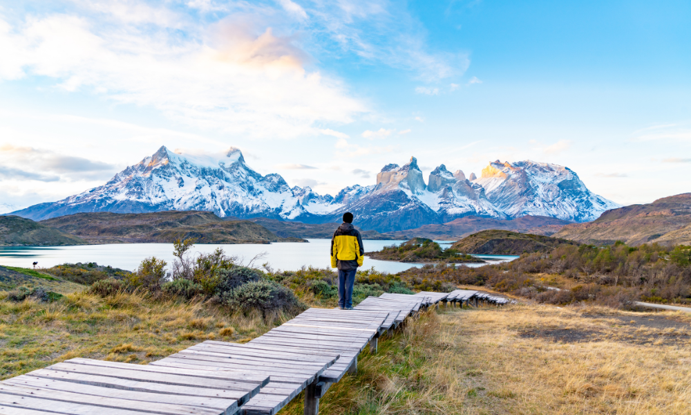 hiker in yellow jacket walking on boardwalk away from camera towards Chilean mountain range