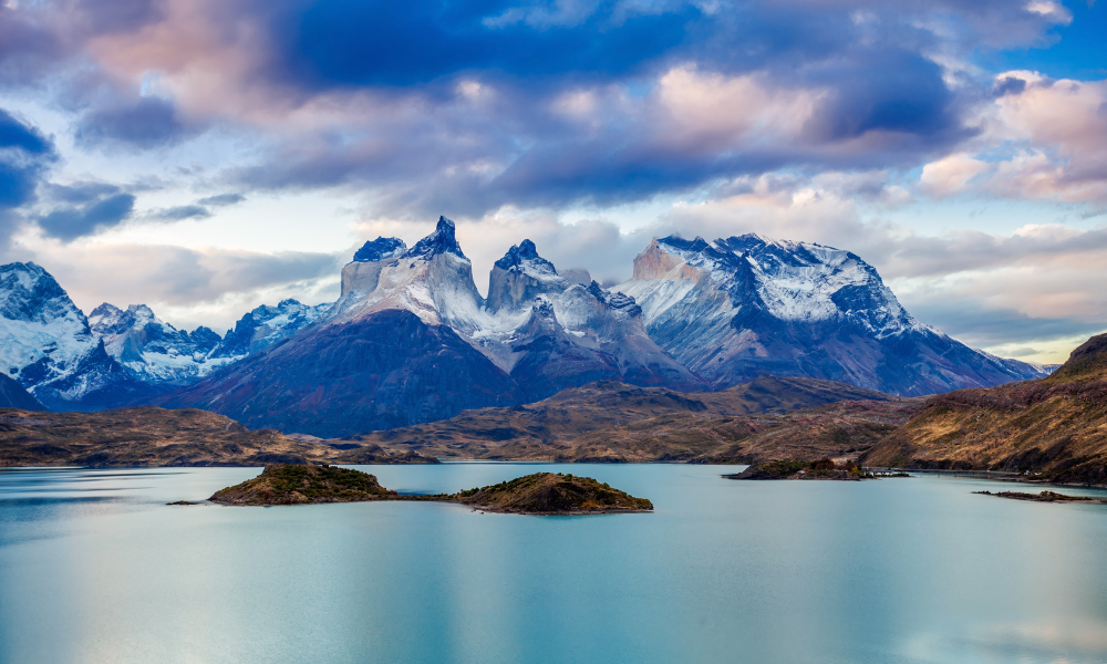 snow capped mountain range in the distance with light blue lake in the foreground