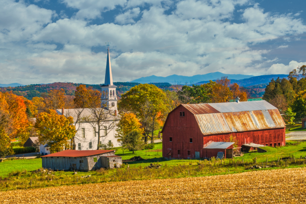 red barn and white church set in front of autumn trees and mountains in vermont