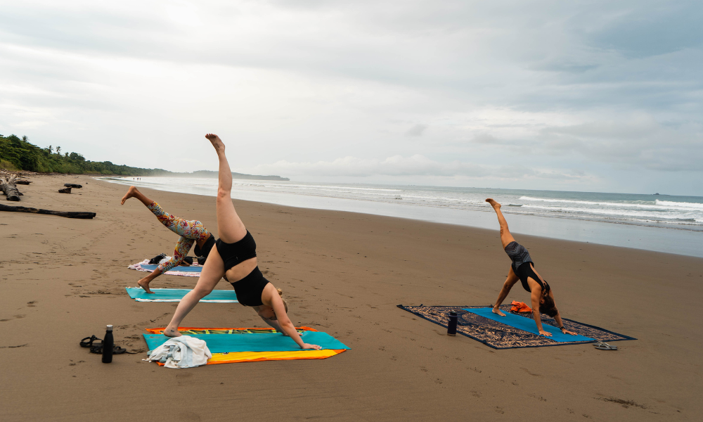three women doing yoga on the beach.