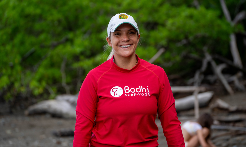 a woman in a red long-sleeved shirt that says "Body Surf + Yoga". She is also wearing a baseball cap.